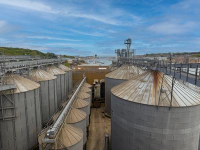 Aerial view of large grain storage silos with a coastal harbour in the background
